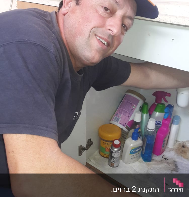 אדם בודק ארון מתחת לכיור עם חומרי ניקוי